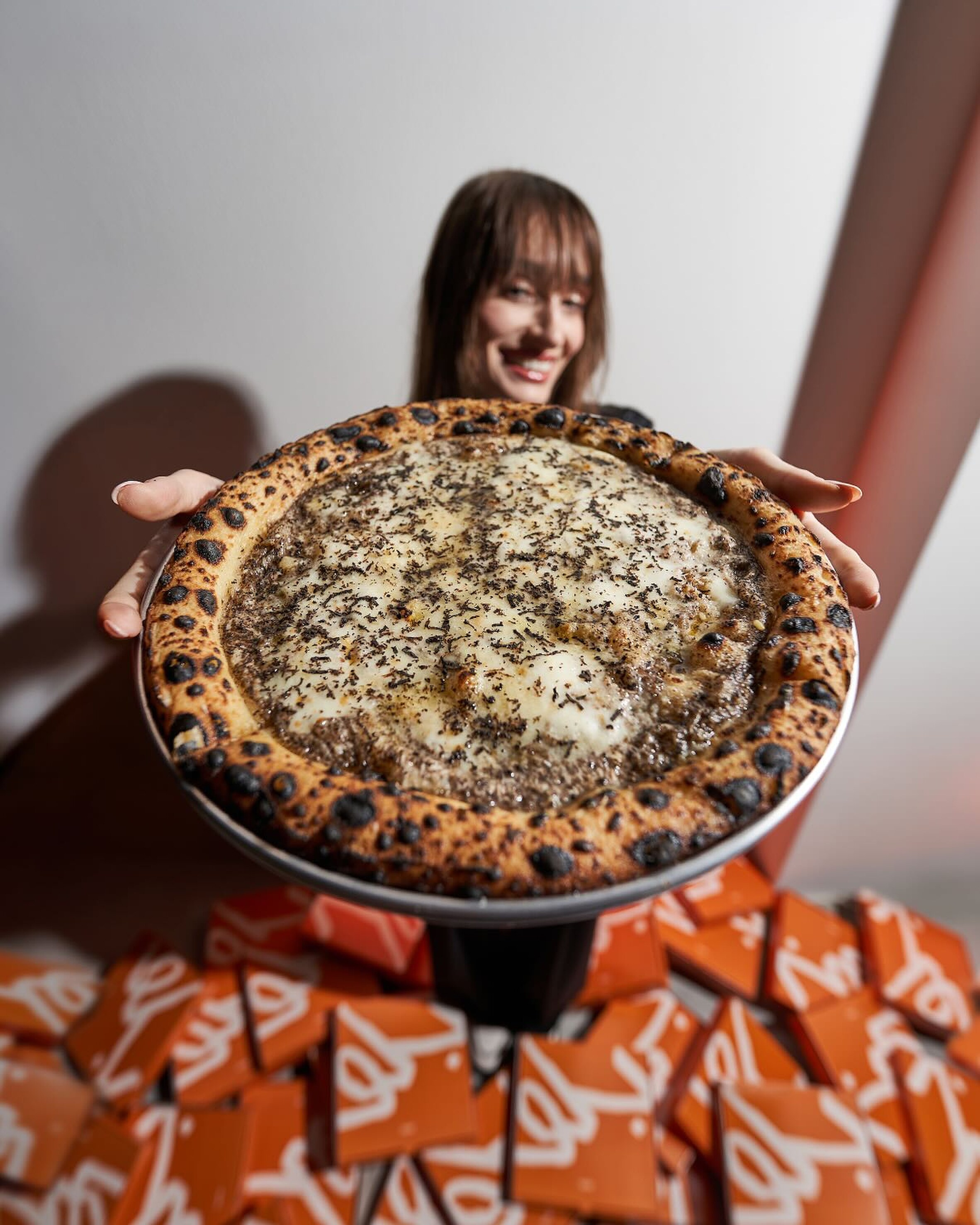 Tartufo pizza held above a sea of orange Blu boxes
